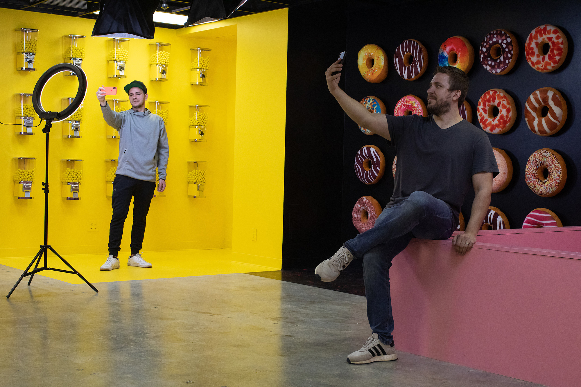 Two men taking selfies in front of colorful backdrops.