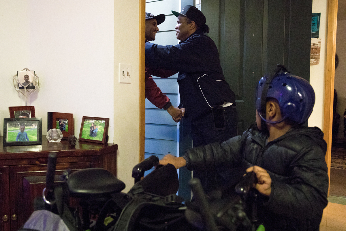 Anthony Battiste shakes a man’s hand at the entrance to his family’s apartment