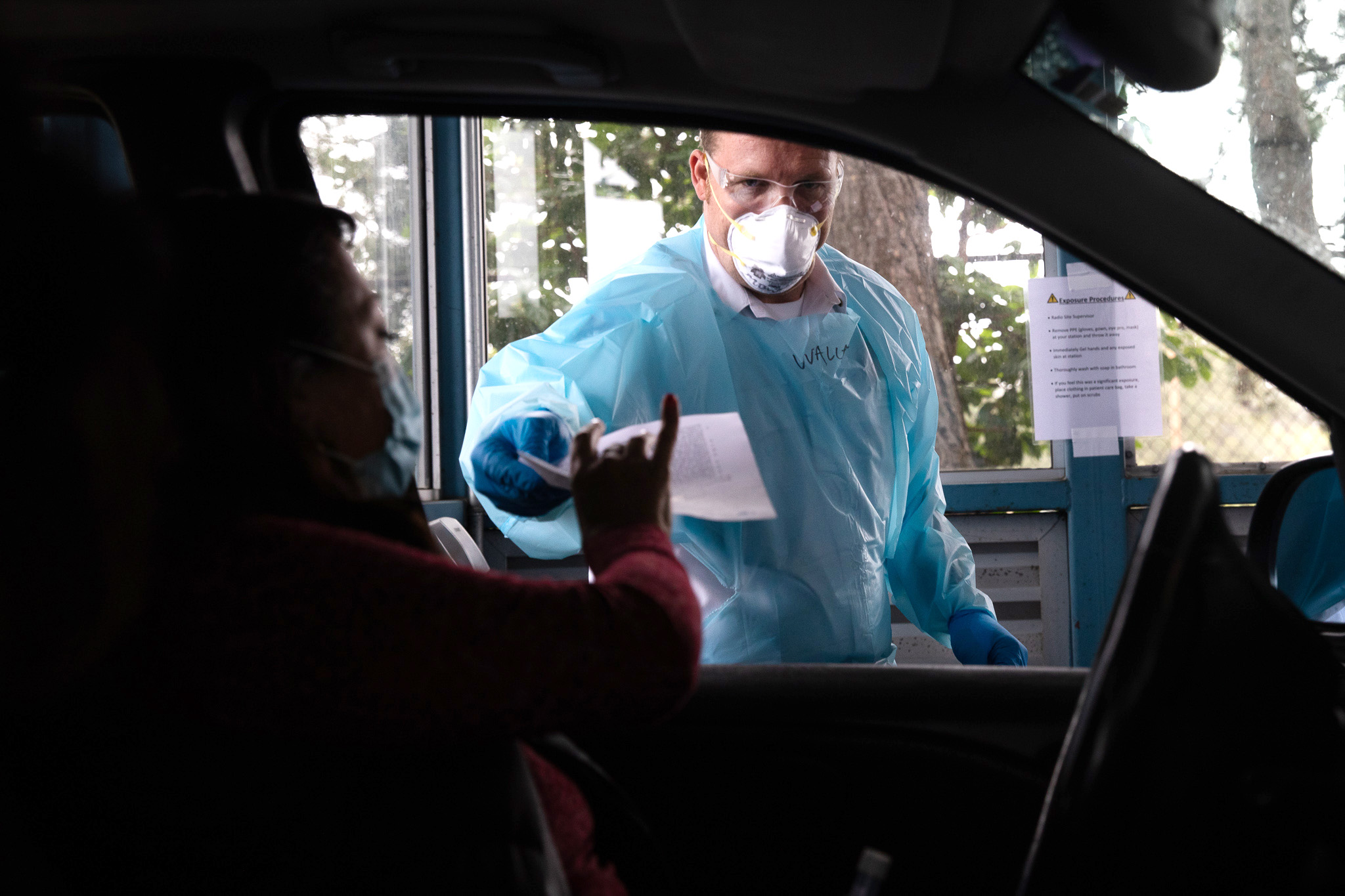 Lt. Brian Wallace of the Seattle Fire Department assists patients at a drive-up COVID-19 testing facility housed at what is normally the Washington State Vehicle Emission Check Program Station 4 in Shoreline, King County, June 12, 2020. "Someone pulled in expecting an emissions test and they were incredibly surprised to find out what it's currently being used for," says Wallace, while helping a patient. Wallace has been in charge of the department's testing operations since the pandemic began. (Matt M. McKnight/Crosscut)