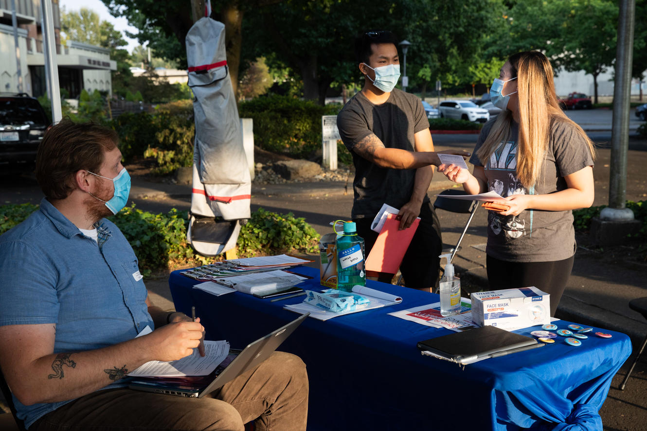 A couple approaches a man seated at a table that's stocked with vaccine information.