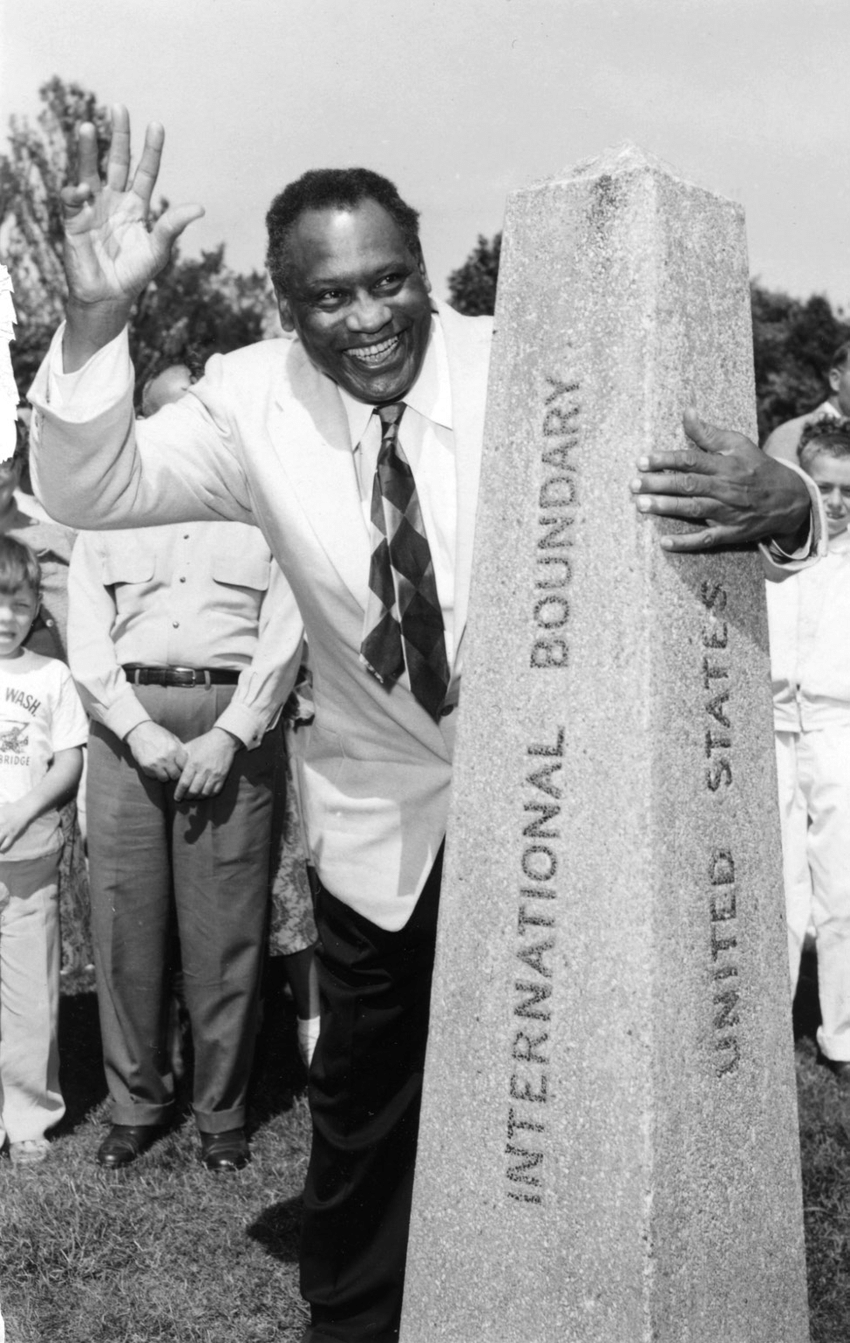 Man waving and holding onto a obelisk with the words “International Boundary” written on it.