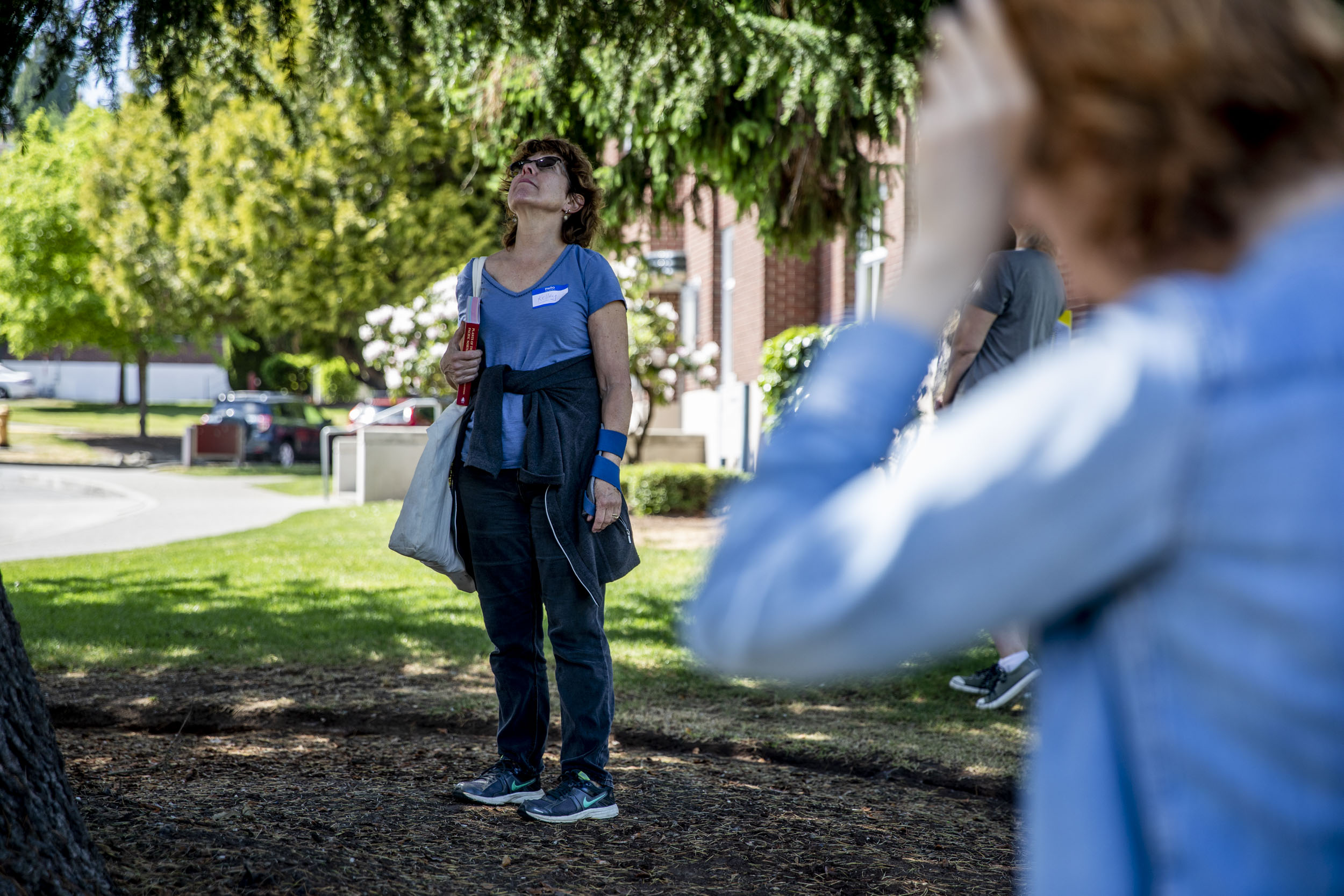 Kelley McHenry of Shoreline looks up into a tree as a group of volunteers learn about identifying majestic or exceptional trees, meaning trees with a trunk diameter of 30 inches or more, at Magnuson Park in Seattle on May 19, 2019. (Photo by Dorothy Edwards/Crosscut)