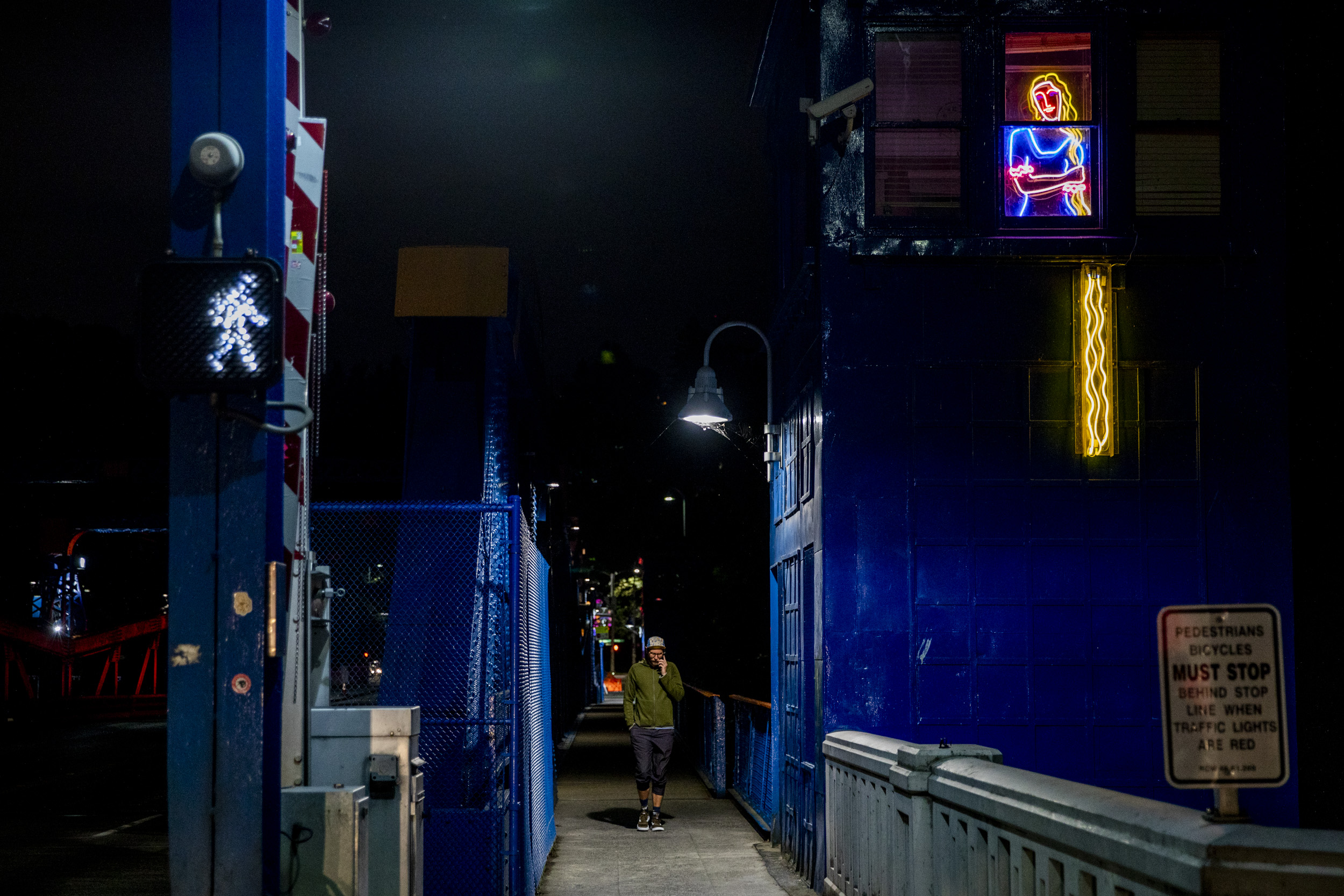 Man walks on bridge passed neon sign