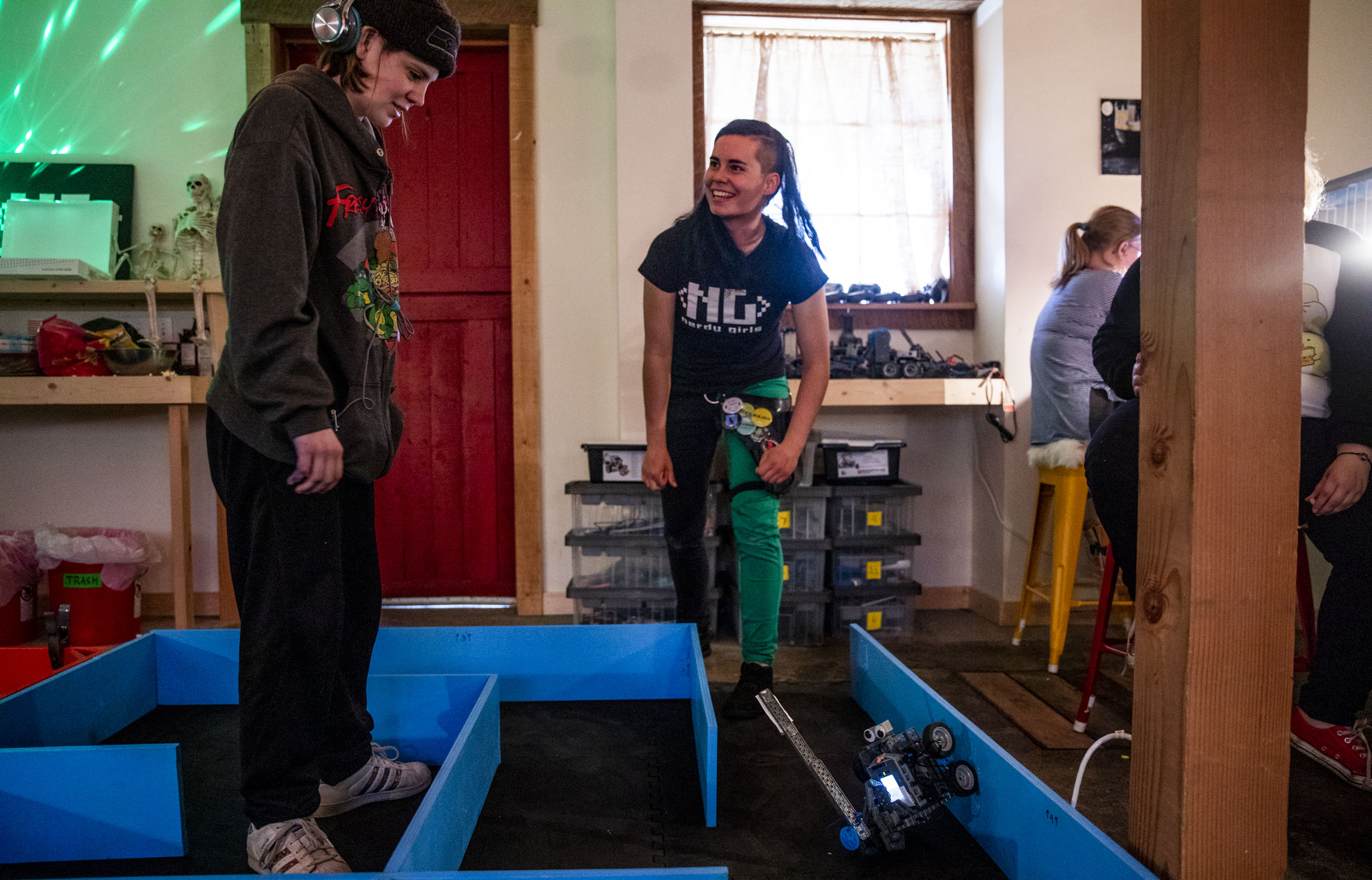 Nerdy Girls co-founder and high school senior Parker Mayer, right, encourages high school freshman Madison "Sparky" Sparks as she tests out her robot in a challenge course during a meetup in the Nerdy Girls barn in Ellensburg on May 17, 2019. (Photo by Dorothy Edwards/Crosscut)