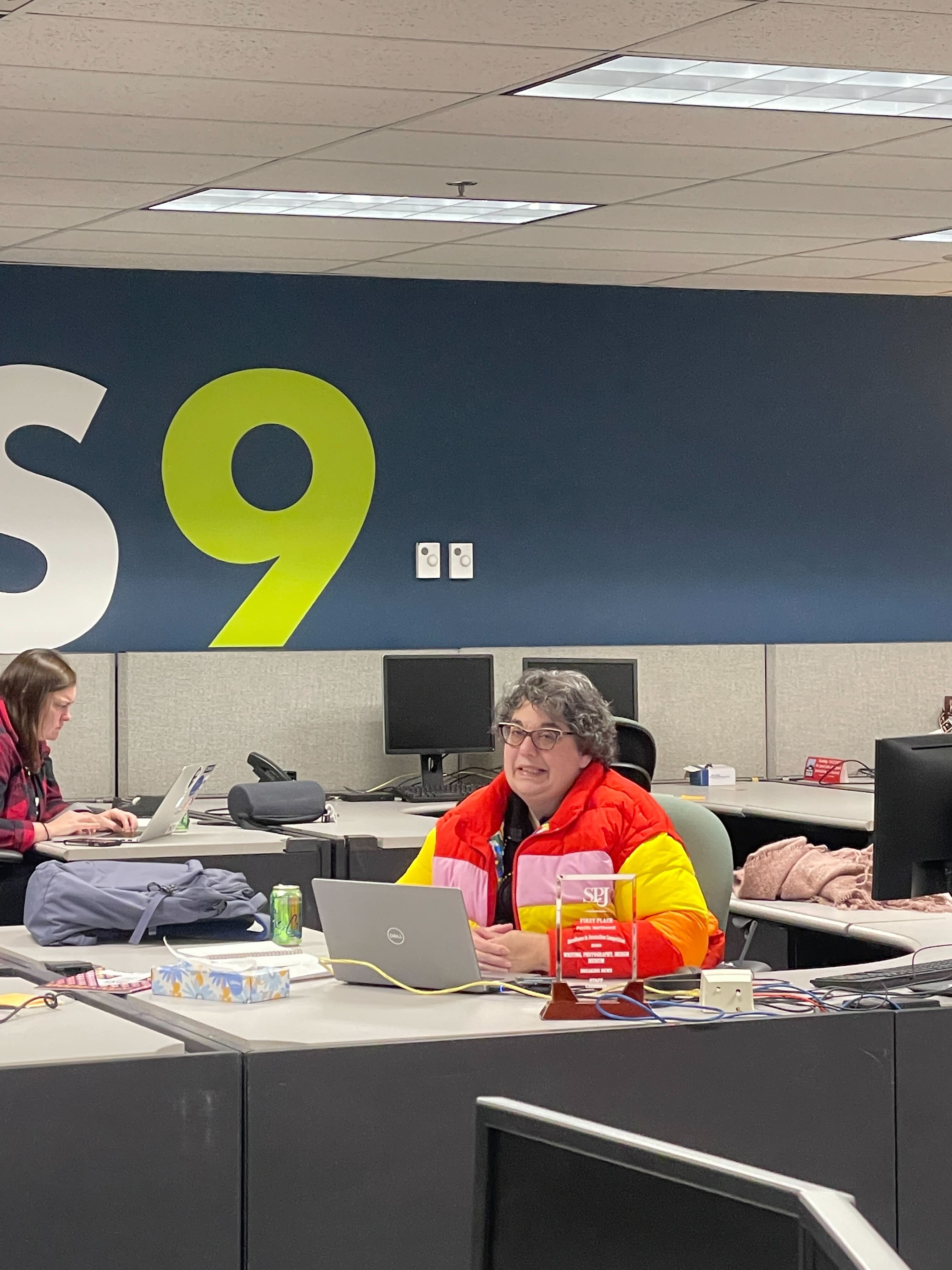 Donna Blankinship sits at her desk in a brightly-colored puffy jacket