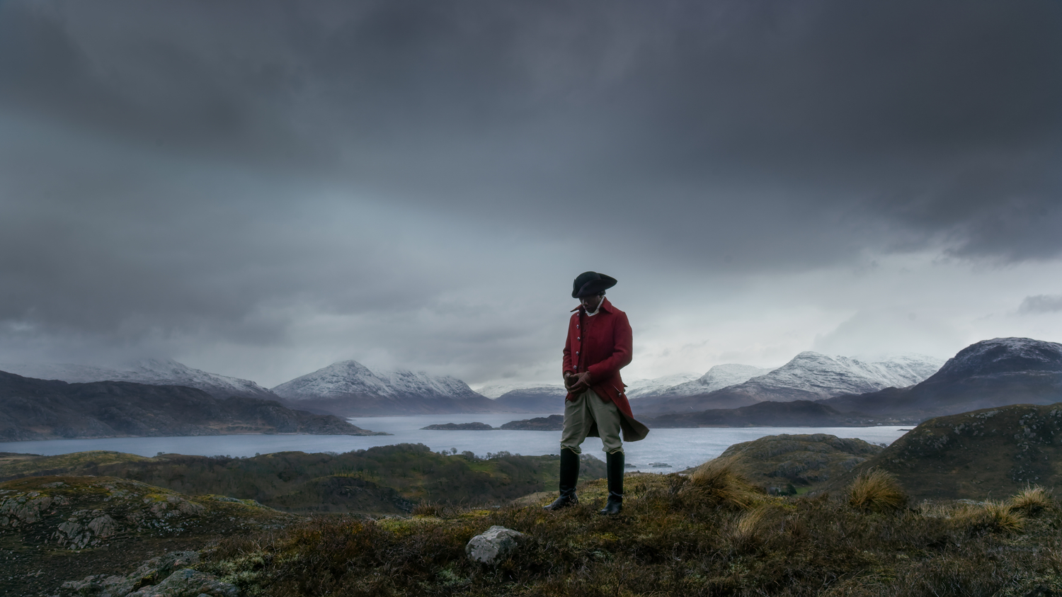 Man in historical dress stands in front of large body of water