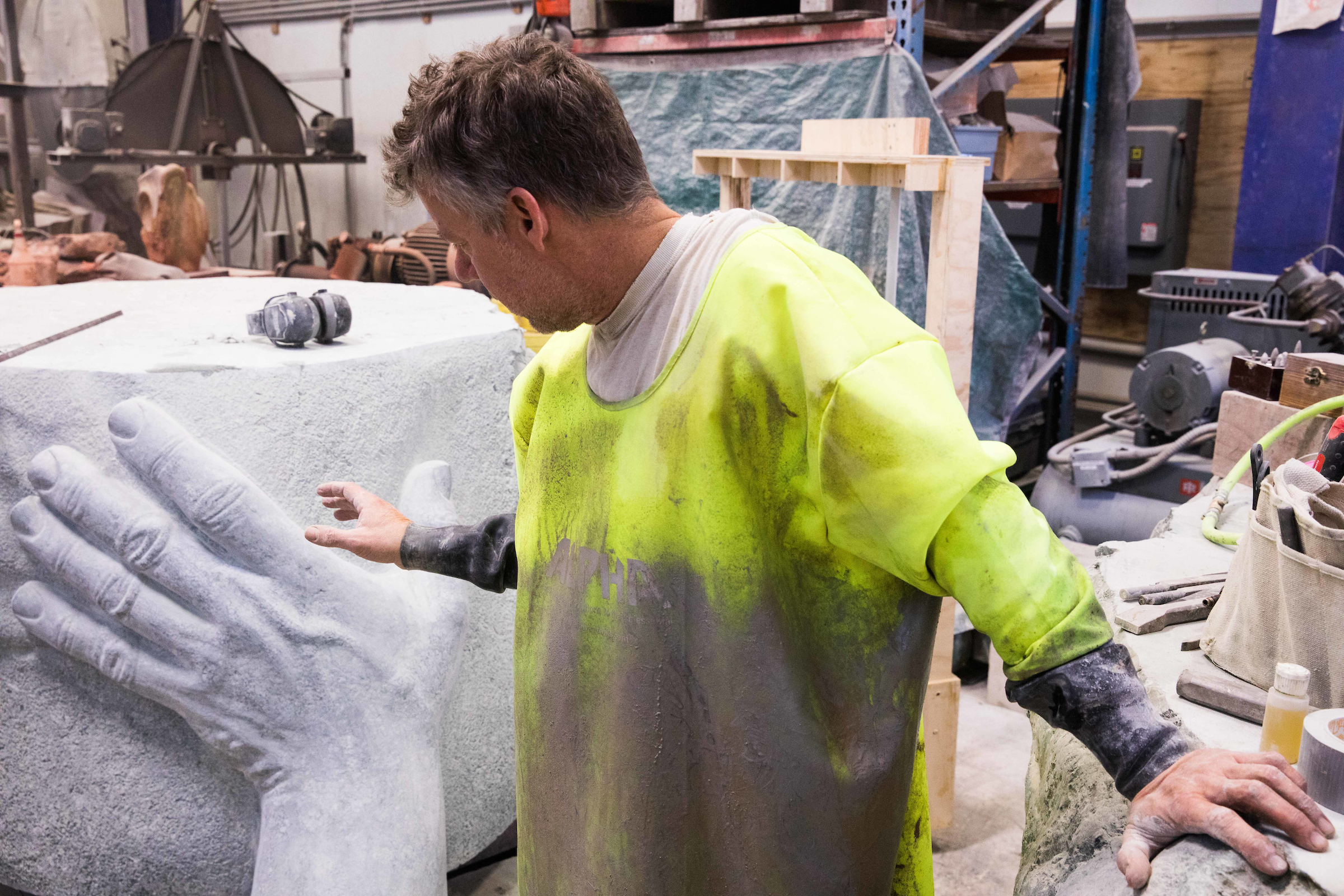 a man in a yellow rubber smock reaches toward a large carved boulder