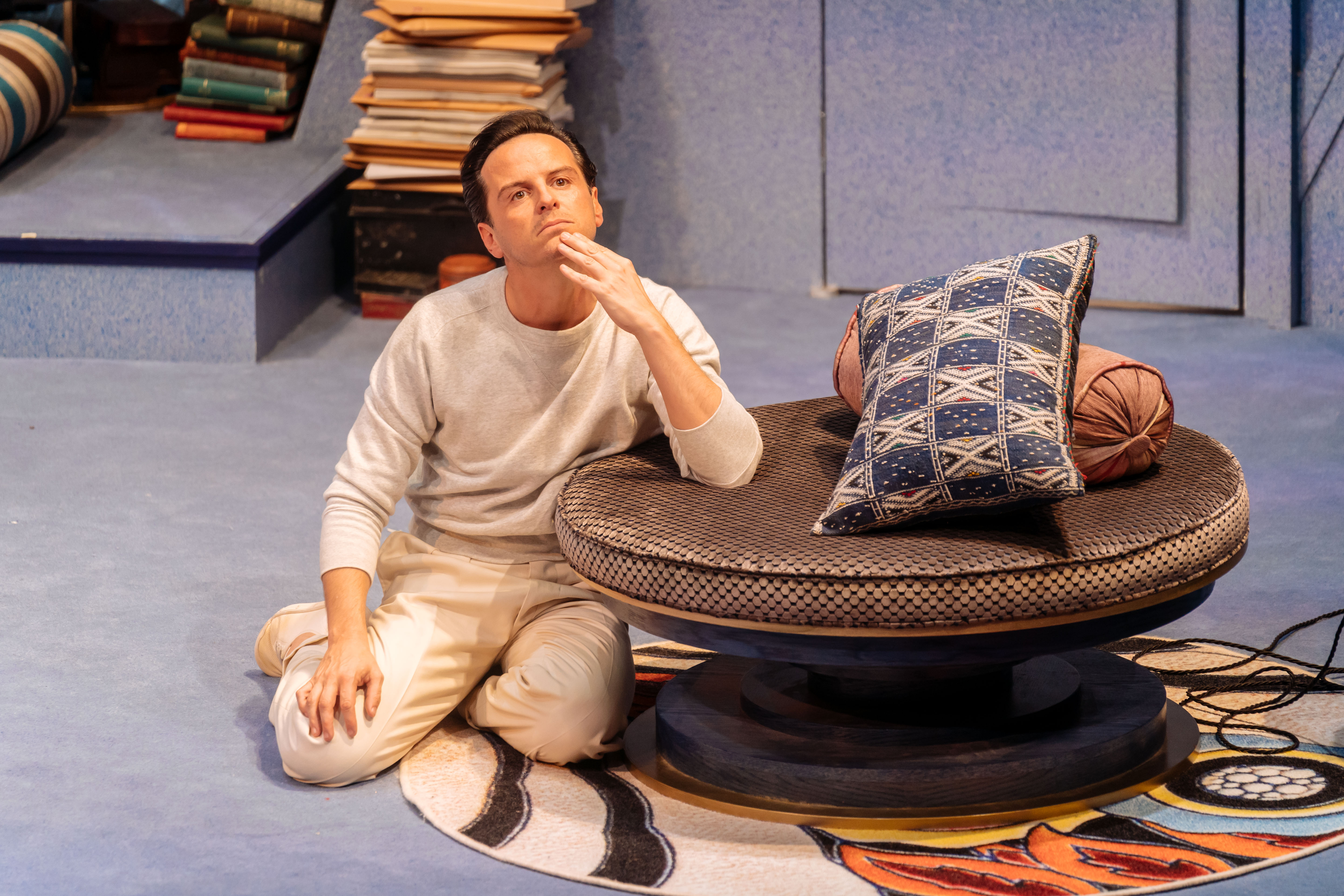 a pensive man on stage, sitting on the floor next to pillows