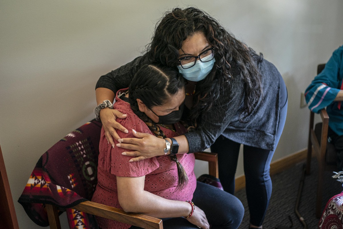 A woman hugs another woman who is sitting