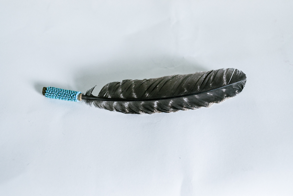 a black feather adorned with blue beadwork