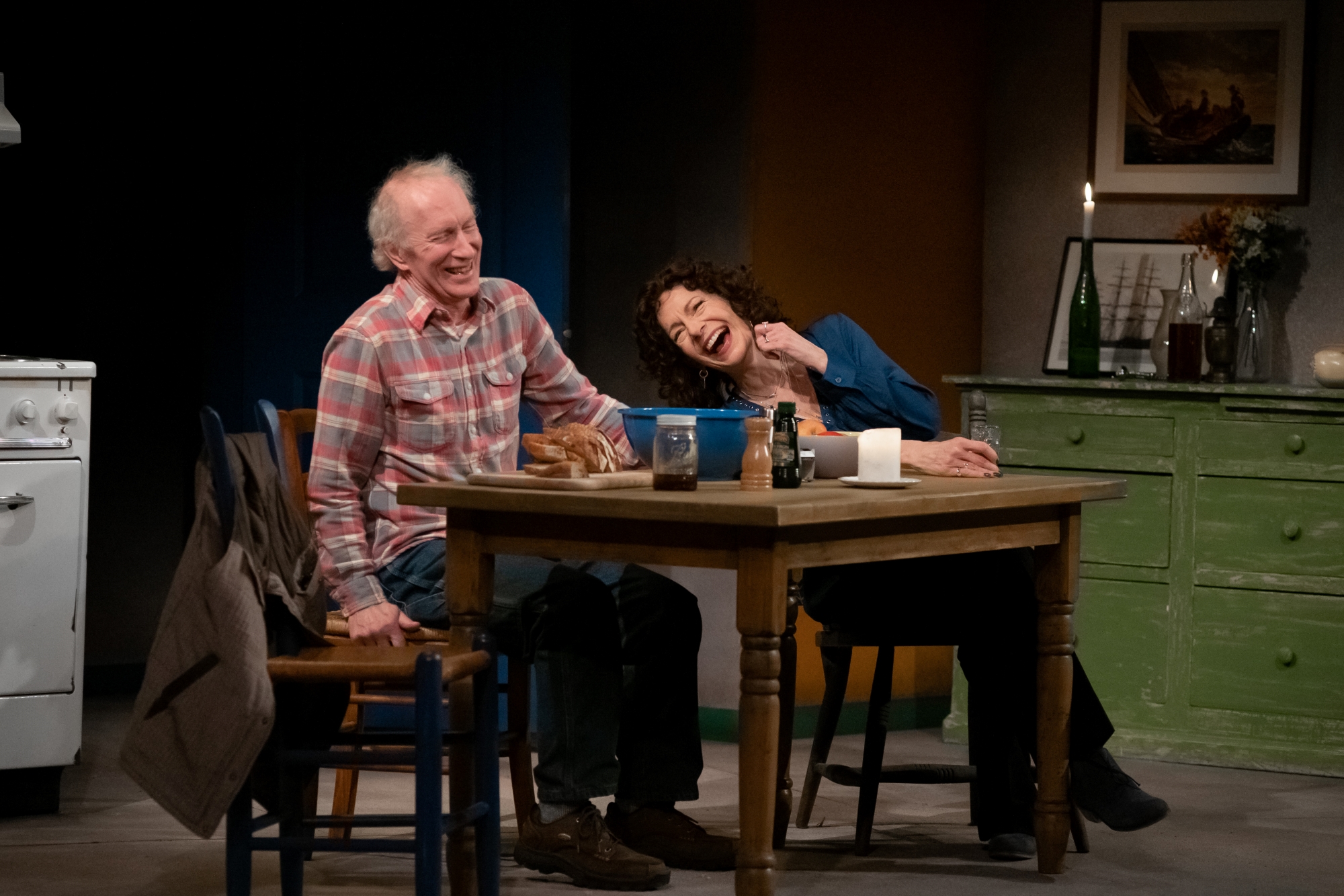 a man and a woman sit at a kitchen table on stage