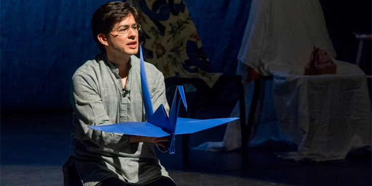 a man on stage holding a blue paper bird