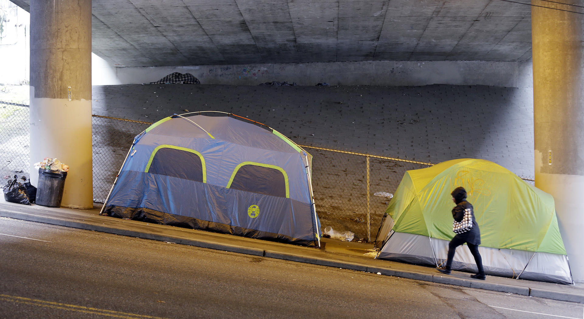 A person walks up a hill next to tents lined up beneath a highway adjacent to downtown Seattle, Wednesday, March 8, 2017. (AP Photo/Elaine Thompson)