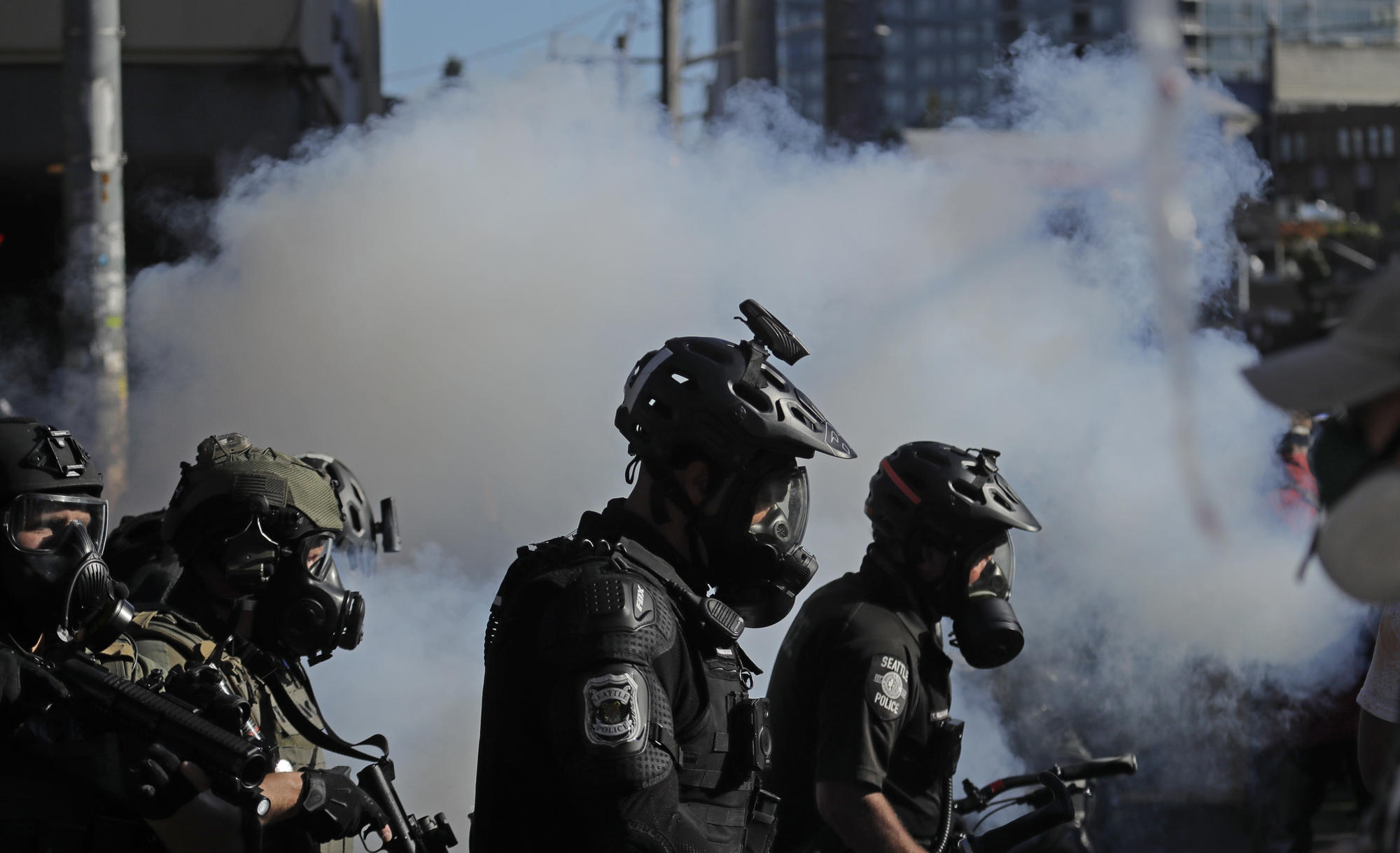 Police officers silhouetted in front of cloud of tear gas