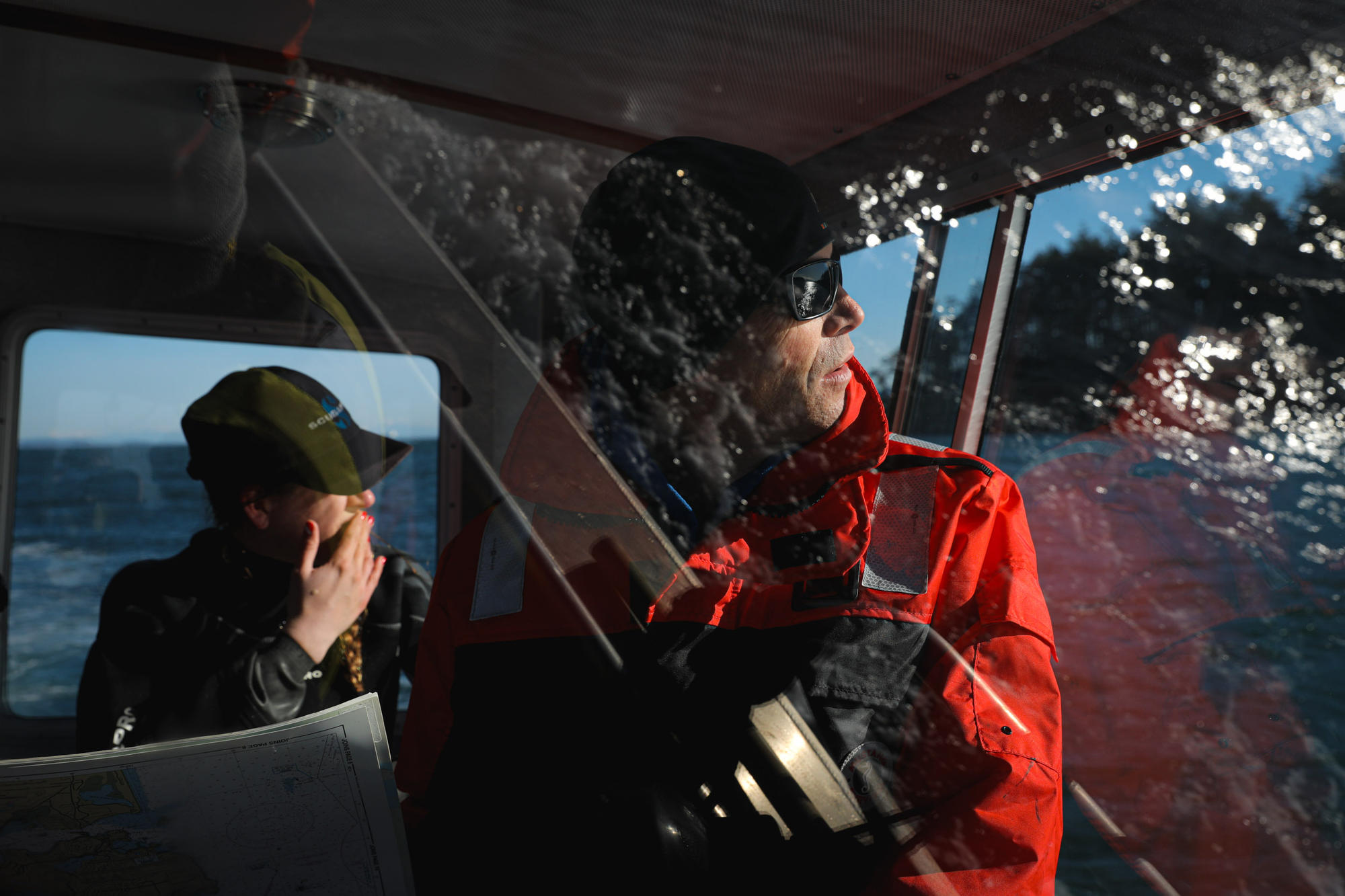 Water is reflected off glass as people inside the cabin of a boat look out toward the water