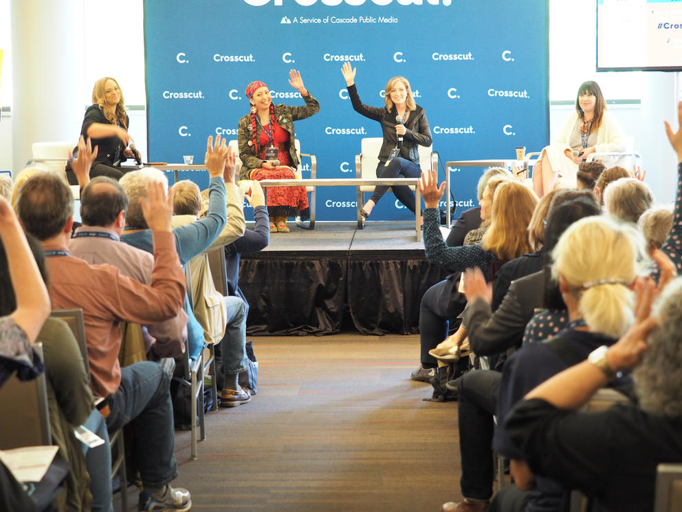 The four panelists raise their hands in front of a crowd.