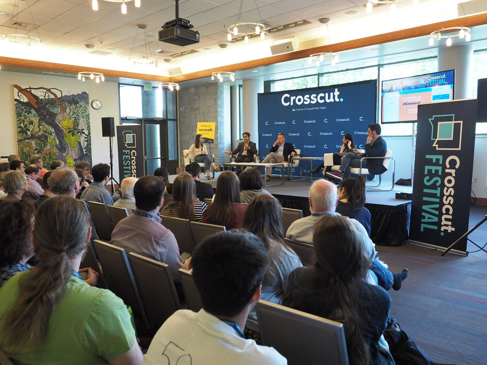 A crowd watches as panelists speak in a light-filled room.