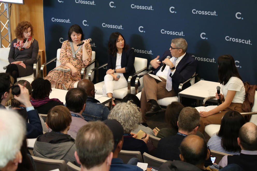 The panelists sit before a crowded room