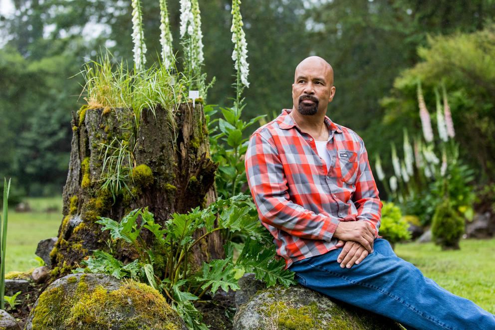 Nathaniel Sanders sits outside on a mossy log