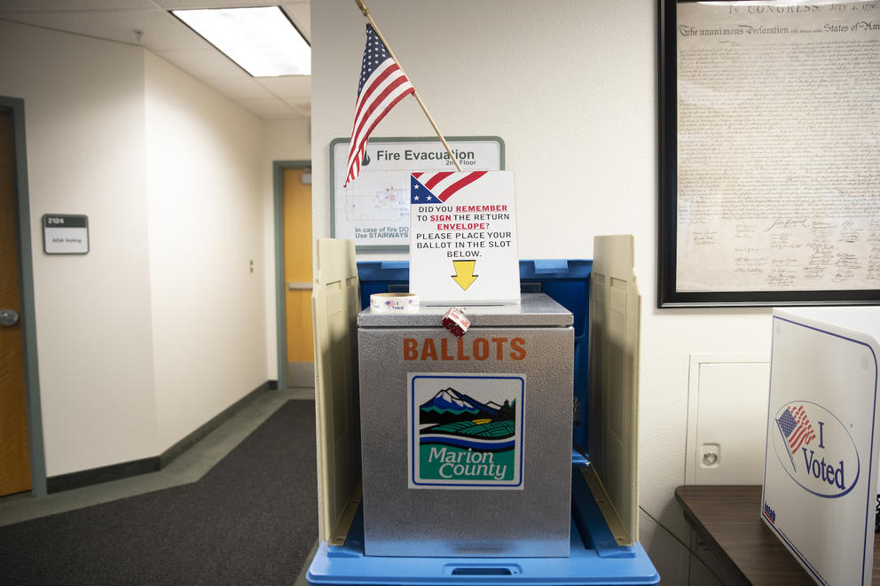 Ballot box with a sign on top that reads "Did you remember to sign the return envelope? Please place your ballot in the slot below"