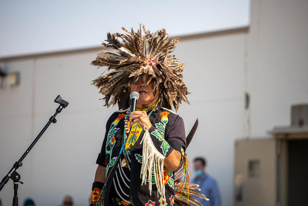 Francis Cullooyah stands in regalia while holding a microphone