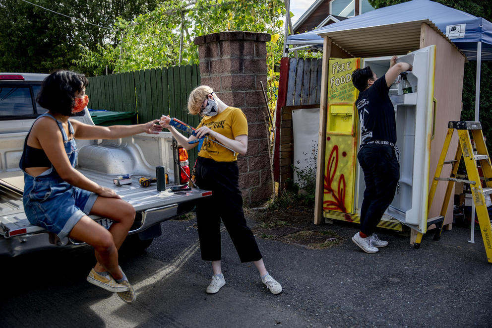 three people on the back of a car and near a tall fridge