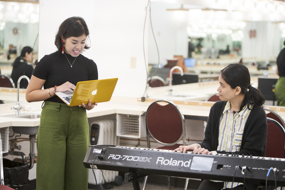 Two people, one carrying laptop, another sitting at key board