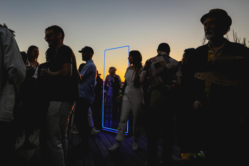 A group of people, shady against the sunset sky, and in the middle a neon blue rectangle 