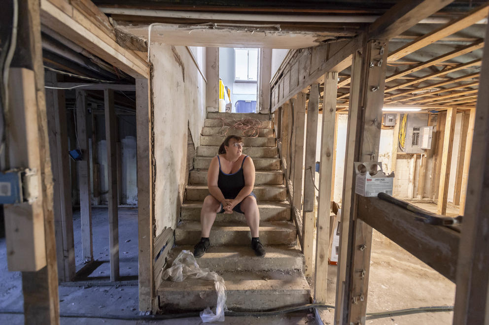 A woman sits on stairs leading down to her basement