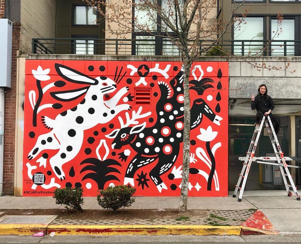 large mural with red background featuring two animals, next to it, on a ladder, the artist