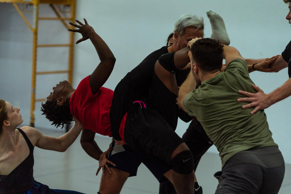 three dancers in a rehearsal spaces touching each other almost like in a fight, caught in motion