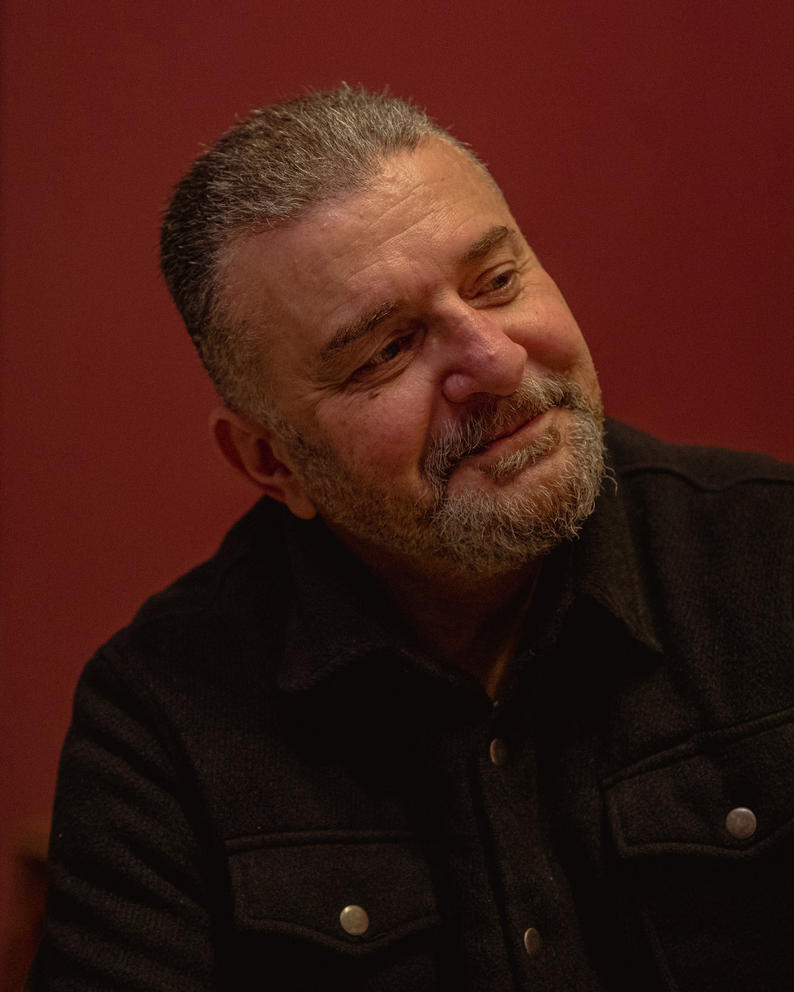 a man with close cropped hair and beard smiles while looking to the side