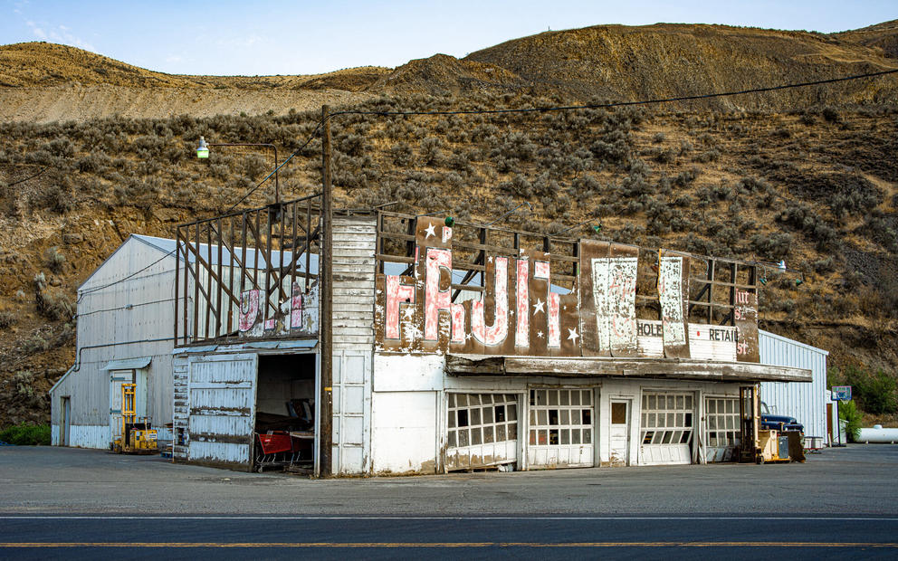 photo of a scrubby landscape with a large, decrepit fruit stand in the foreground