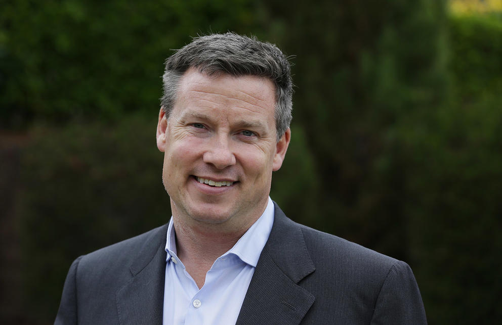 Mark Mullet smiles in a portrait against a dark green background.