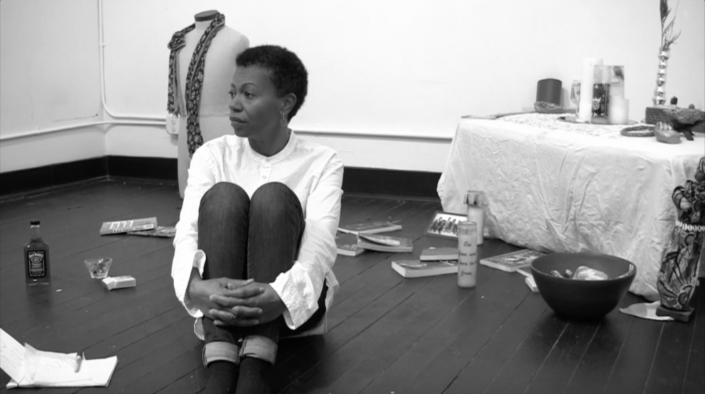 Person in white shirt sitting on dark floor with arms wrapped around legs, black and white photo