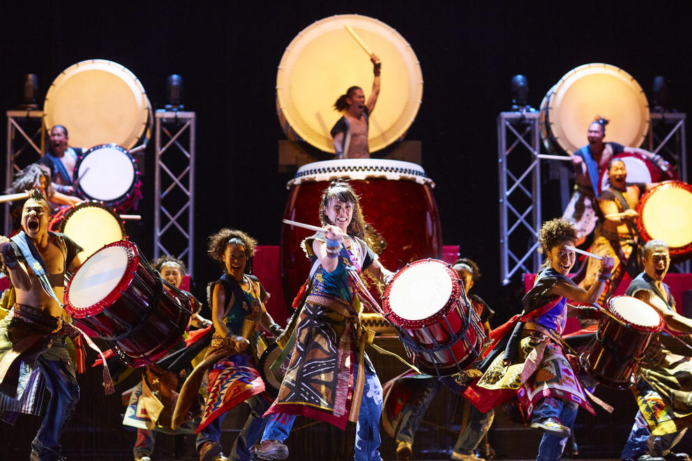 A group of drummers is standing on a stage as they perform