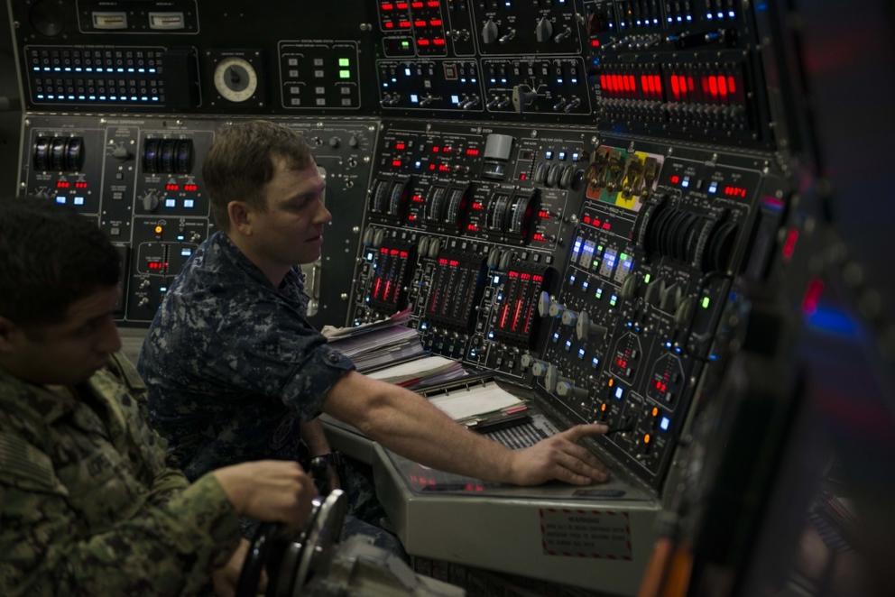 One man flips a switch on a large control panel while another turns a wheel.