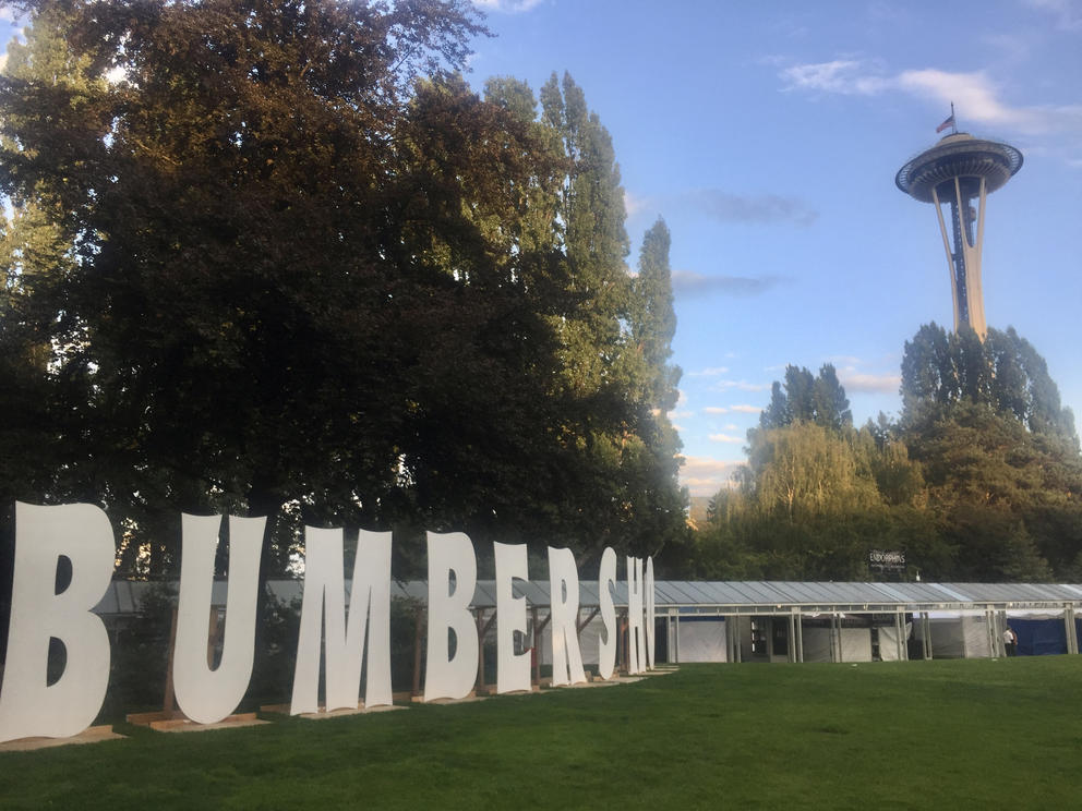 Seattle Center grounds with Space Needle in the distance and large cardboard letters spelling out BUMBERSHOOT