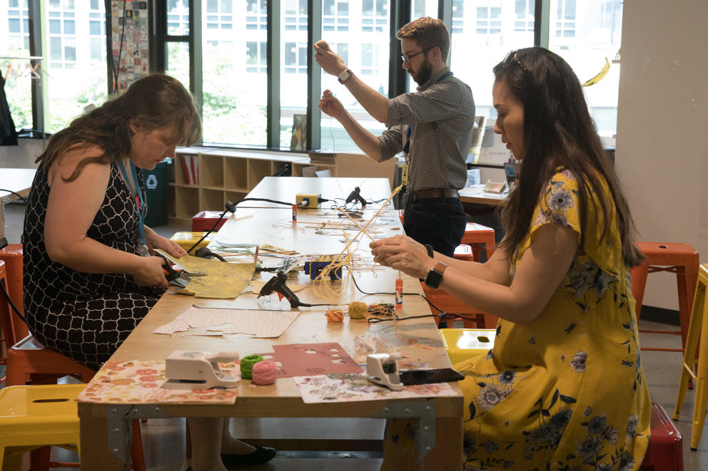 Three people cutting paper and making crafts at a table