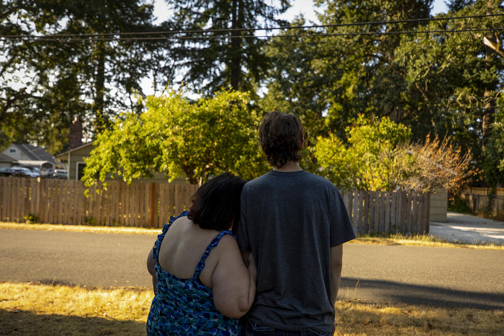 A woman and young man hug facing a wooded scene