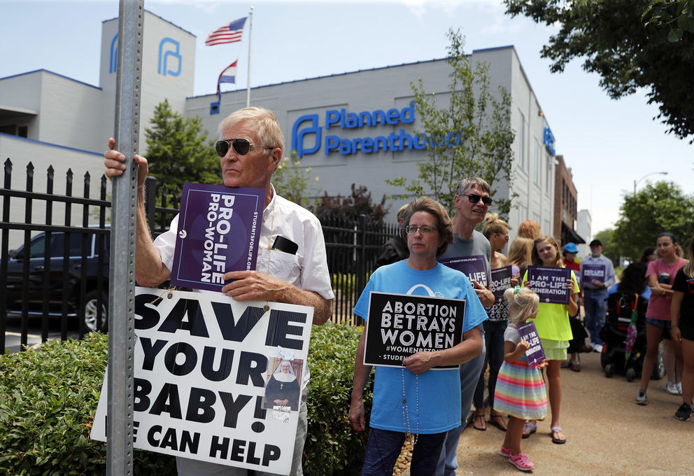 A line of protesters hold signs reading "Pro-life Pro-woman," "Abortion betrays women," and "Save your baby! We can help"