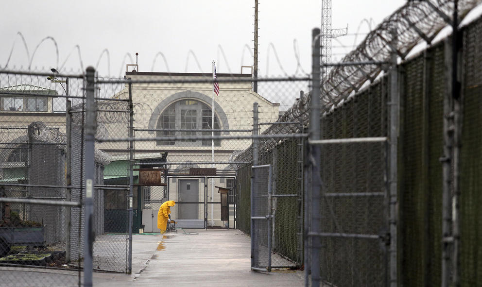 A man in yellow rain gear cleans a walkway to a prison gate.