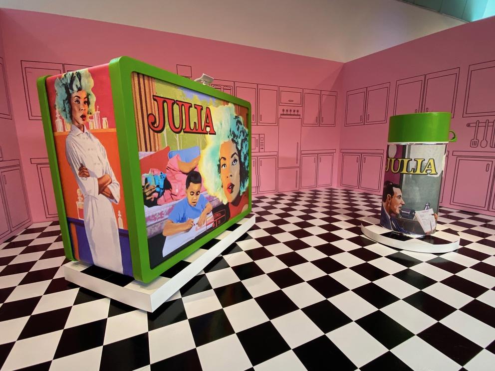 Large checker-board floor in a pink room with a giant lunch box and thermos on top