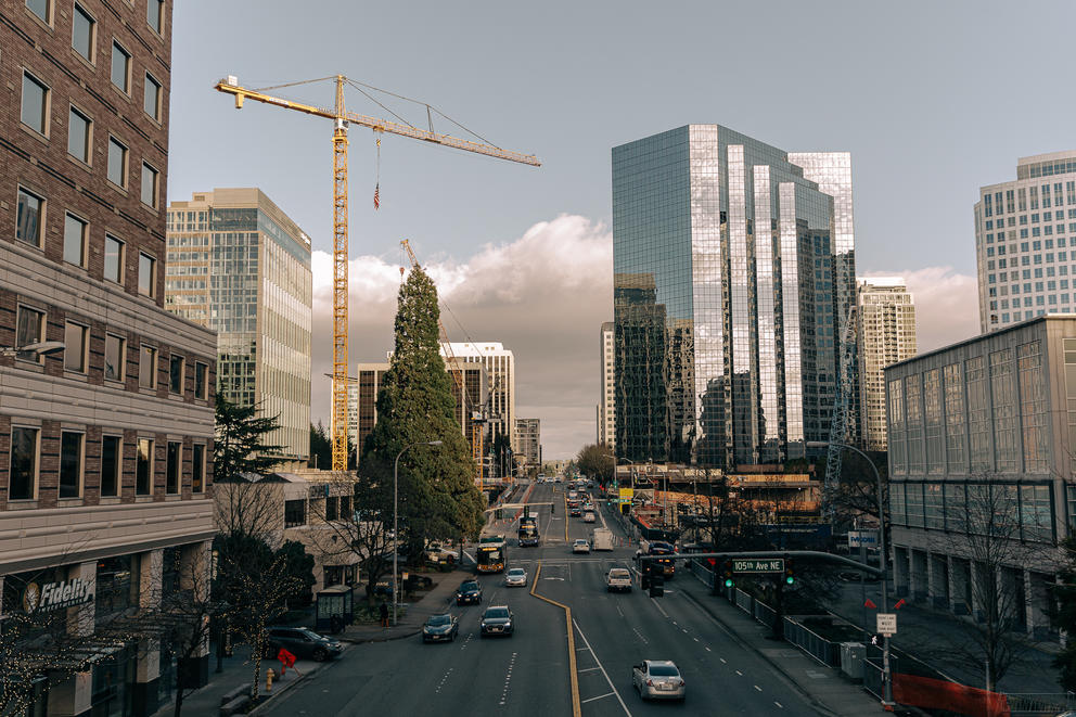 a view down a city street with cars, tall buildings and a large crane rise above both sides of the street