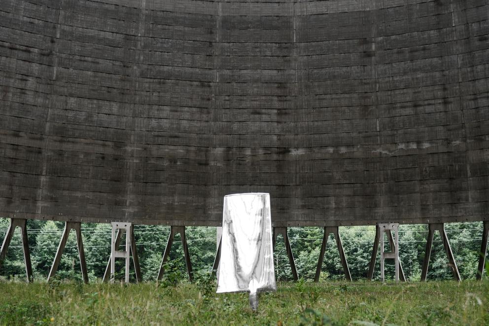 a single chrome blade stands in the grass below a massive structure