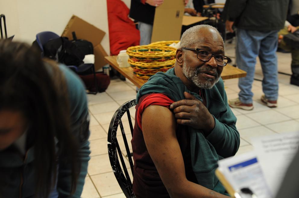 A man sitting in a chair rolls up his sleeve to get a shot.