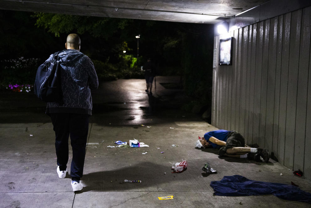 A man walks by a man sleeping on ground