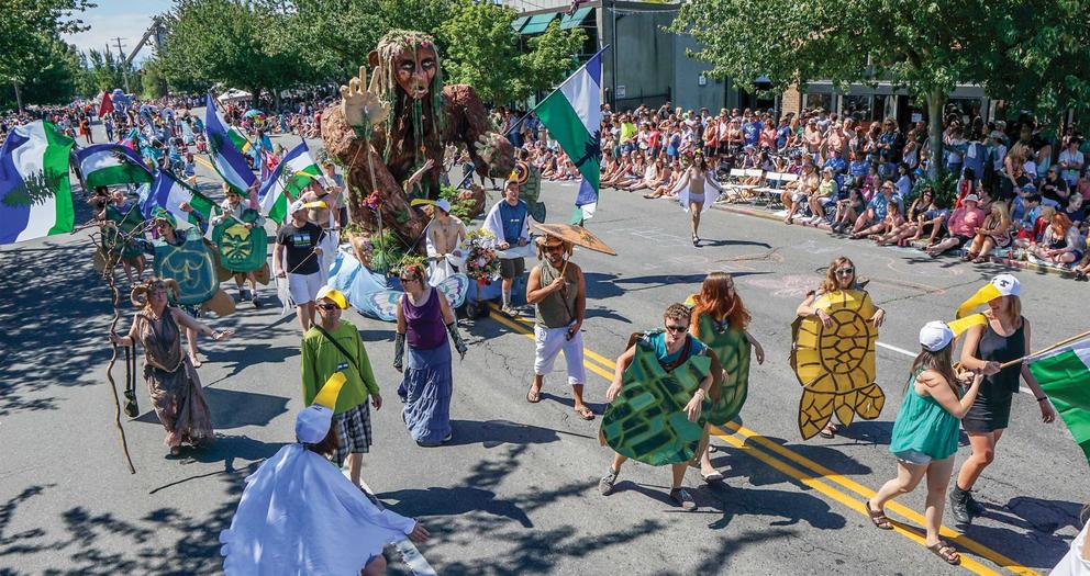 people in a parade wearing turtle costumes with a giant puppet behind them