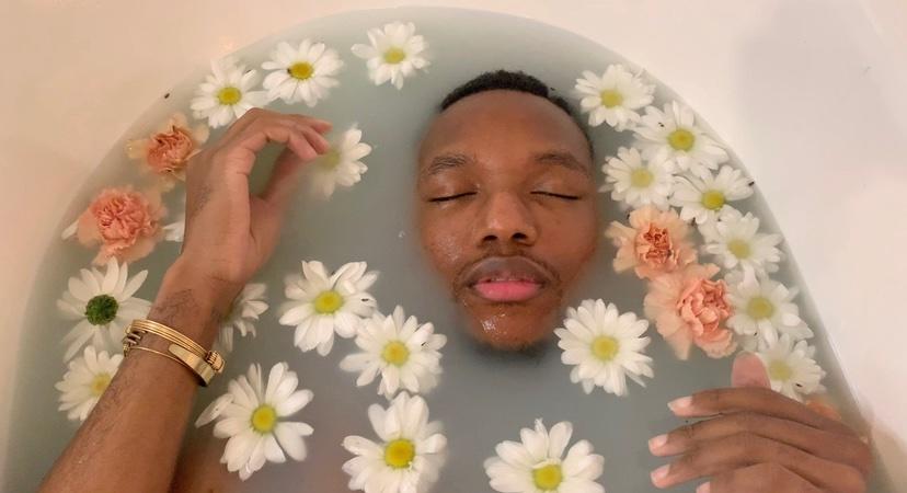 Person in bathtub half submerged, surrounded by floating flowers