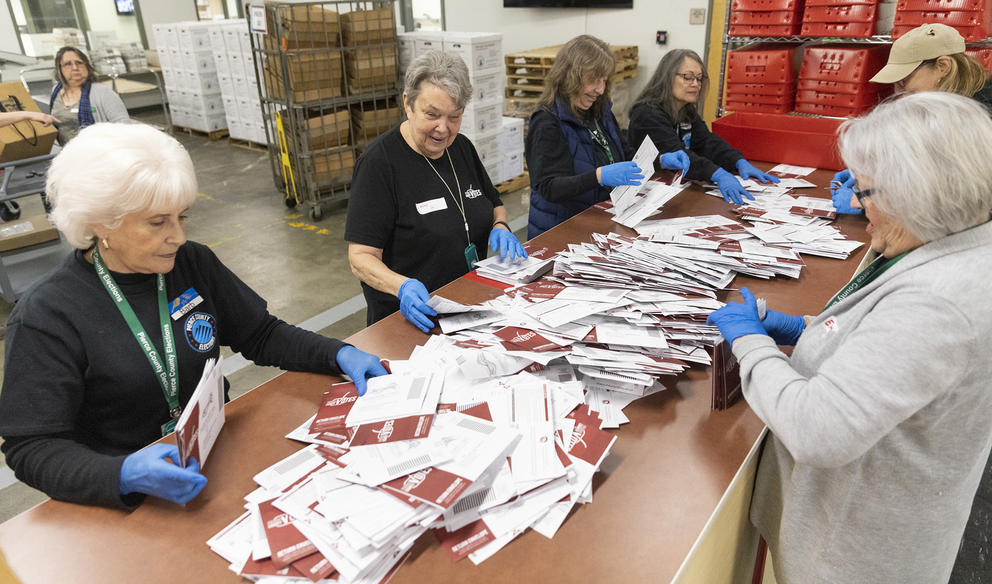 A group of women stand around a table sorting through ballots